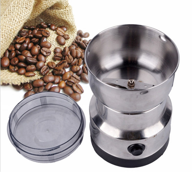 Electric coffee grinder with stainless grinding chamber and lid, coffee beans nearby