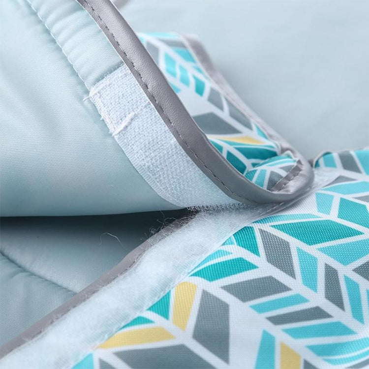 Close-up of waterproof changing pad fabric with teal geometric print and gray binding seam.