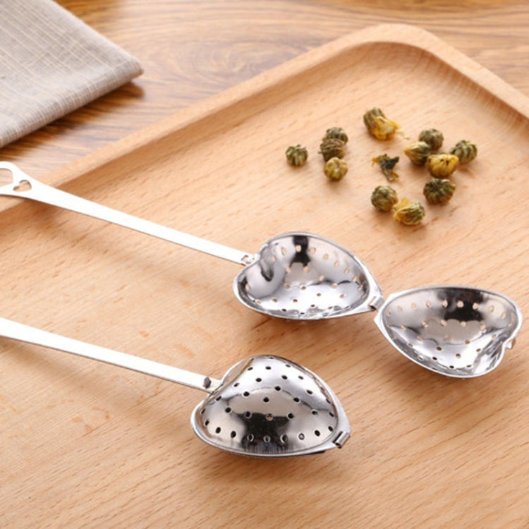 Two heart-shaped stainless tea infuser spoons with dried tea leaves on a board