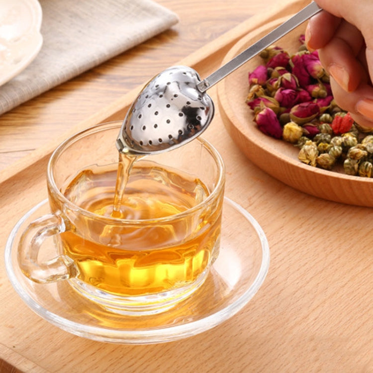 Hand holding heart-shaped stainless tea infuser spoon above a cup of tea