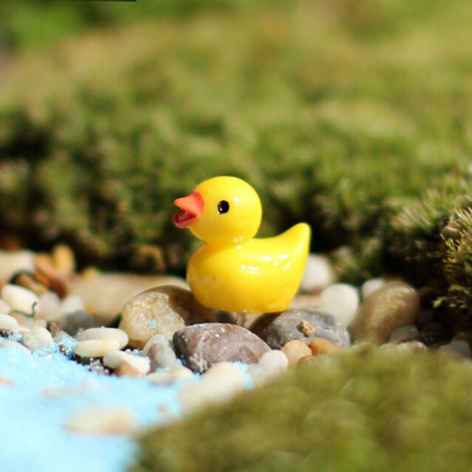 Yellow resin duck figurine sitting on green moss and small pebbles