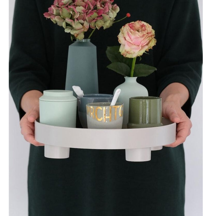 Hands holding round storage tray with wide rim, white base feet, decorative jars