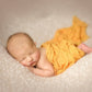 Newborn lying on a white positioning cushion with an orange fabric wrap prop