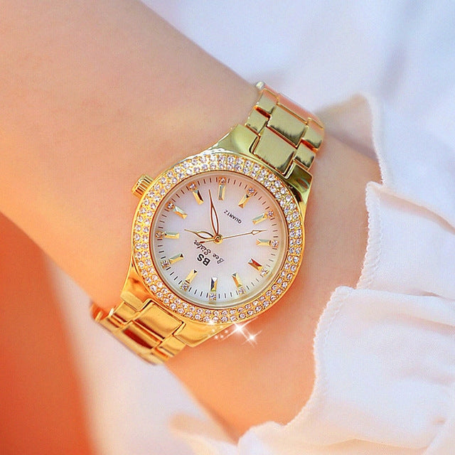 Women’s gold-tone round watch with white dial, sparkling bezel, and metal link bracelet