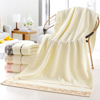 Cream cotton bath towel with gold ornate border, neatly folded on display.