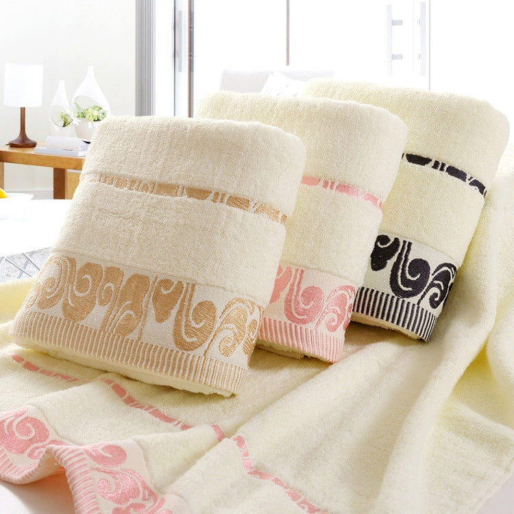 Cream cotton bath towels with pink ornate border trim, stacked for display.