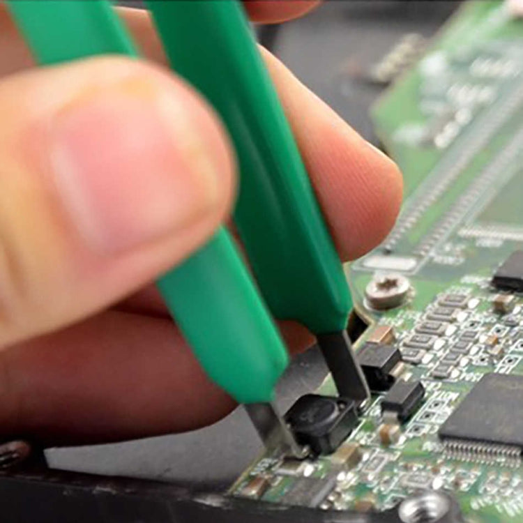 Green tweezers with black jaw tips gripping an IC on a circuit board