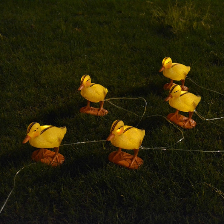 Glowing yellow duck solar lights on stakes with orange bases and connected wires