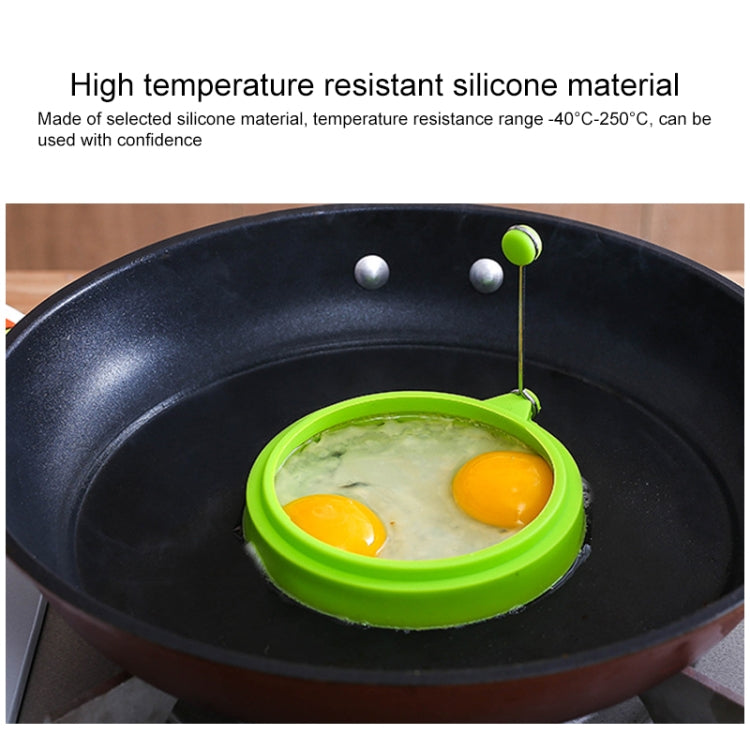 Green round silicone egg ring mold in skillet with two fried eggs.