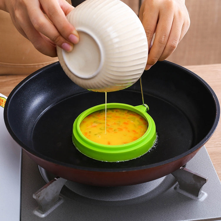 Green round silicone egg ring mold in skillet, batter poured into ring.