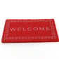 Red dollhouse welcome floor mat with 'WELCOME' lettering and decorative edge