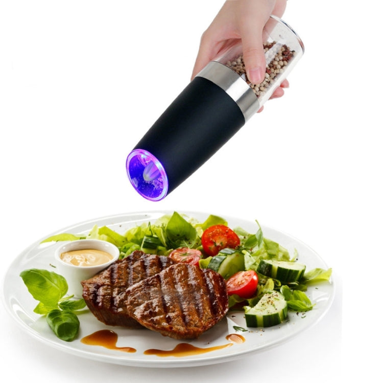 Black electric pepper grinder with purple LED dispensing spices onto a plated meal