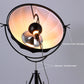 Black circular-shade floor lamp close-up with glowing bulb and adjustment button