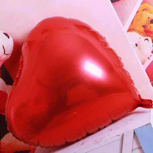 Red heart-shaped foil balloon, glossy surface on white ledge.