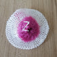 Round mesh gauze pad with white outer ring and purple-pink center on wood surface