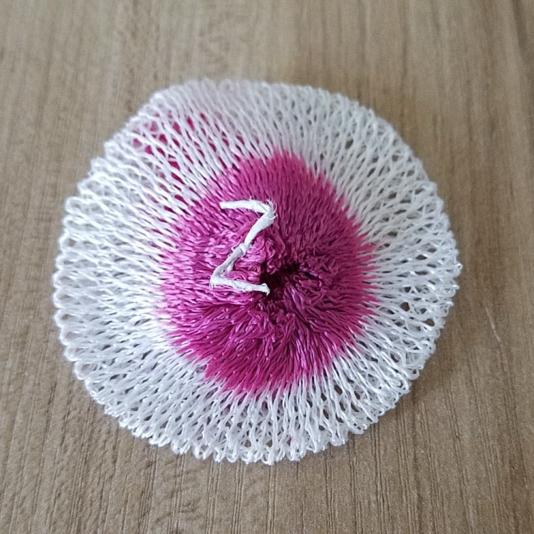 Round mesh gauze pad with white outer ring and purple-pink center on wood surface