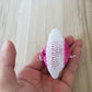 Single mesh gauze pad held in hand, white with magenta-pink center and stitched ring