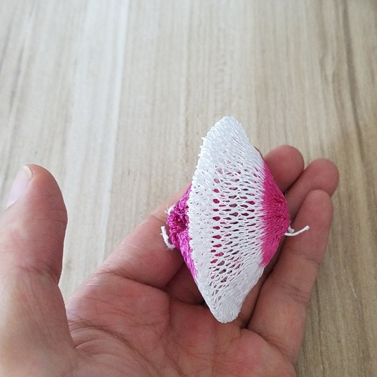 Single mesh gauze pad held in hand, white with magenta-pink center and stitched ring