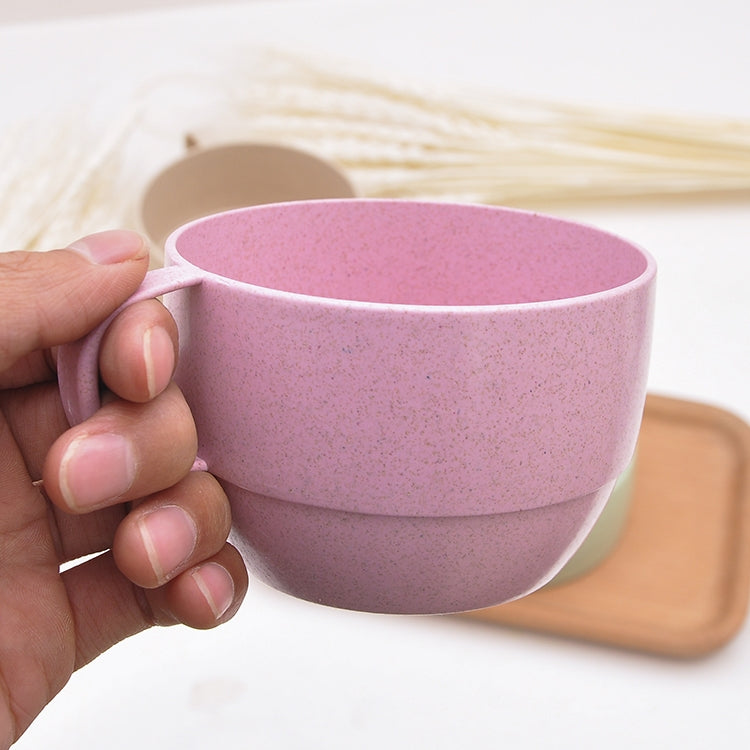 Pink wheat straw coffee cup with handle, held in hand, speckled texture.