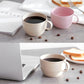 Beige wheat straw coffee cup with handle, dark coffee inside on table.