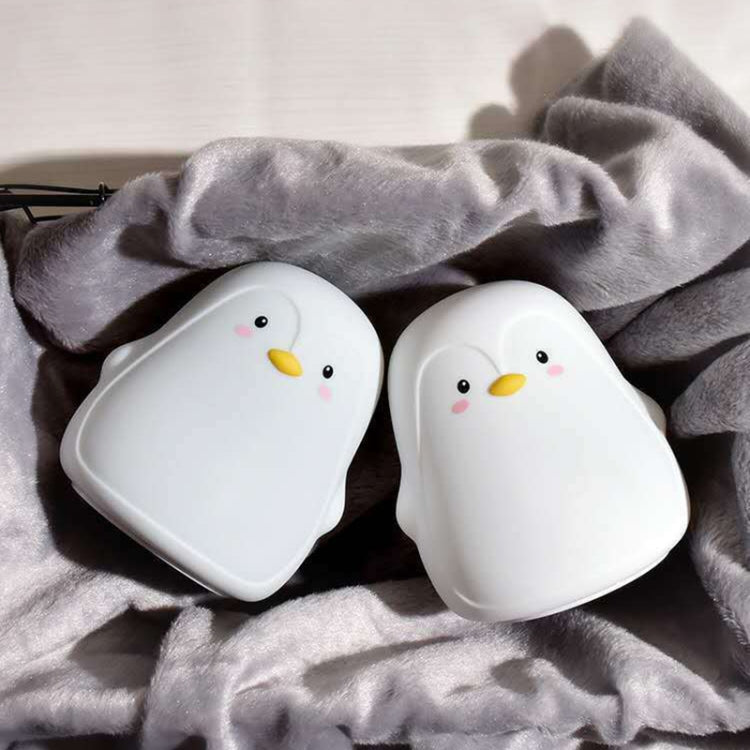 Gray penguin-shaped silicone night light pair on soft gray fabric.