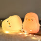 Two glowing penguin-shaped silicone night lights in warm yellow and peach tones.