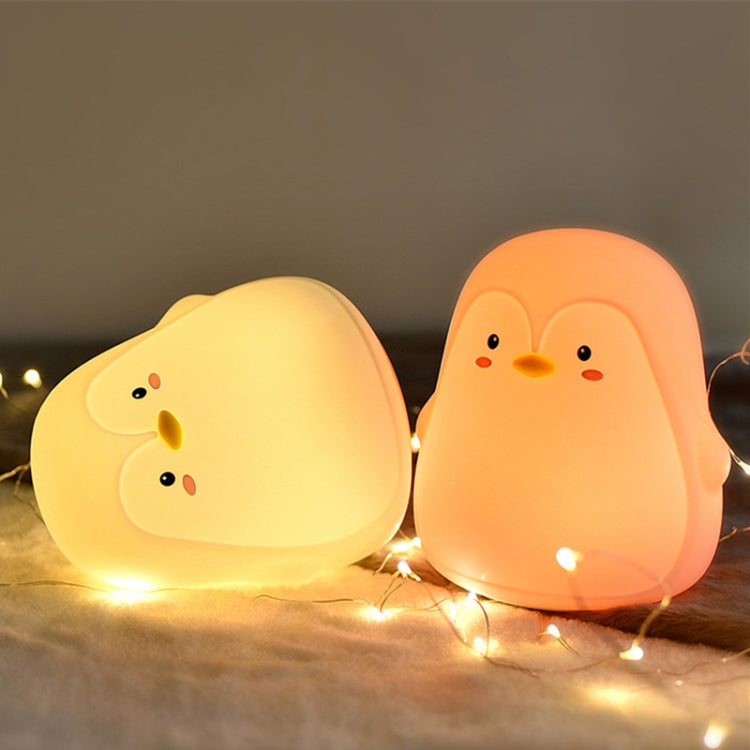 Two glowing penguin-shaped silicone night lights in warm yellow and peach tones.