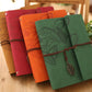 Stacked vintage photo albums in red, orange, and green with leaf embossing and ties.