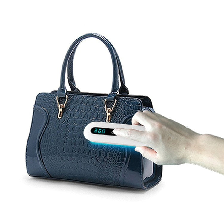 Handheld UV sterilizer wand with blue light over a dark blue handbag