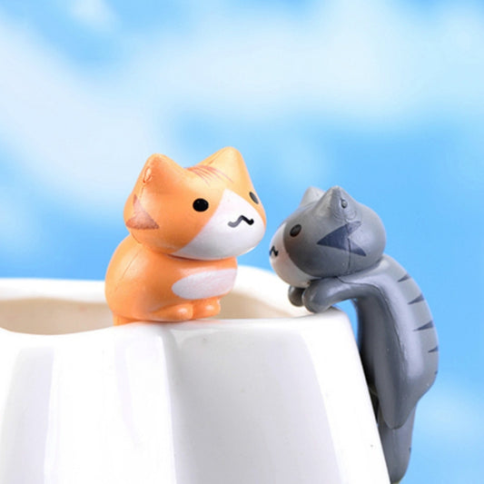 Two cute cat figurines, orange and gray, resting on a white block