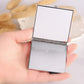 Closed mini folding cosmetic mirror with silver metal frame, held in a hand