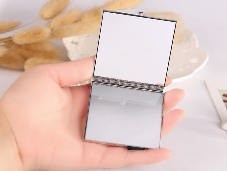 Closed mini folding cosmetic mirror with silver metal frame, held in a hand