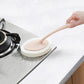 Handheld sponge brush cleaning kitchen counter near stovetop, pink circular pad