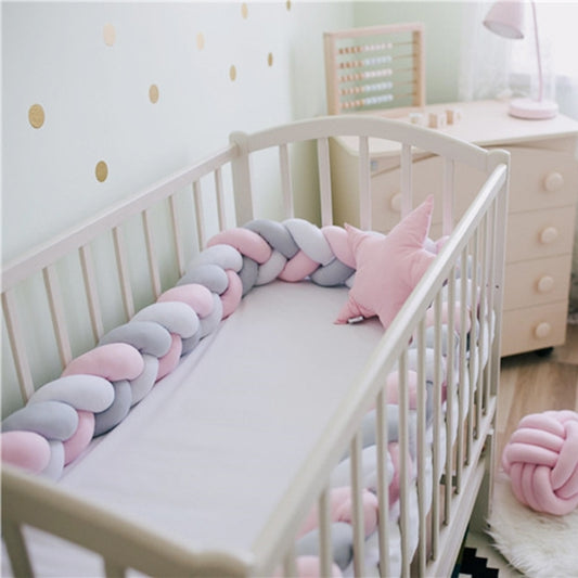 Braided crib bumper along cot rail, pink and gray knot-cord padding