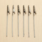 Set of metal wire rope alligator clips with silver jaws on wood surface