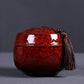 Red ceramic mini tea storage can with glossy lid and hanging tassel pull cord.