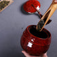 Red ceramic mini tea storage can with open top as a spoon dips into tea.
