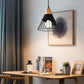 Modern pendant light with black metal cage shade, wood cap, and glowing bulb.