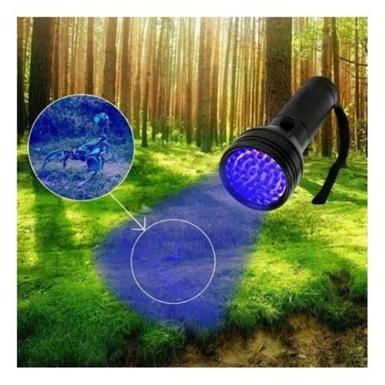 Black UV flashlight with purple UV beam aimed at outdoor grass